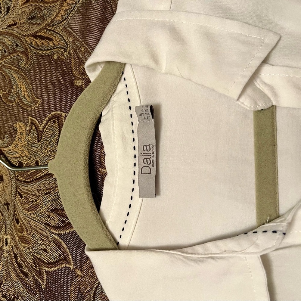 Sleeveless white top. Patch pockets black topstitch inside collar. Extra button